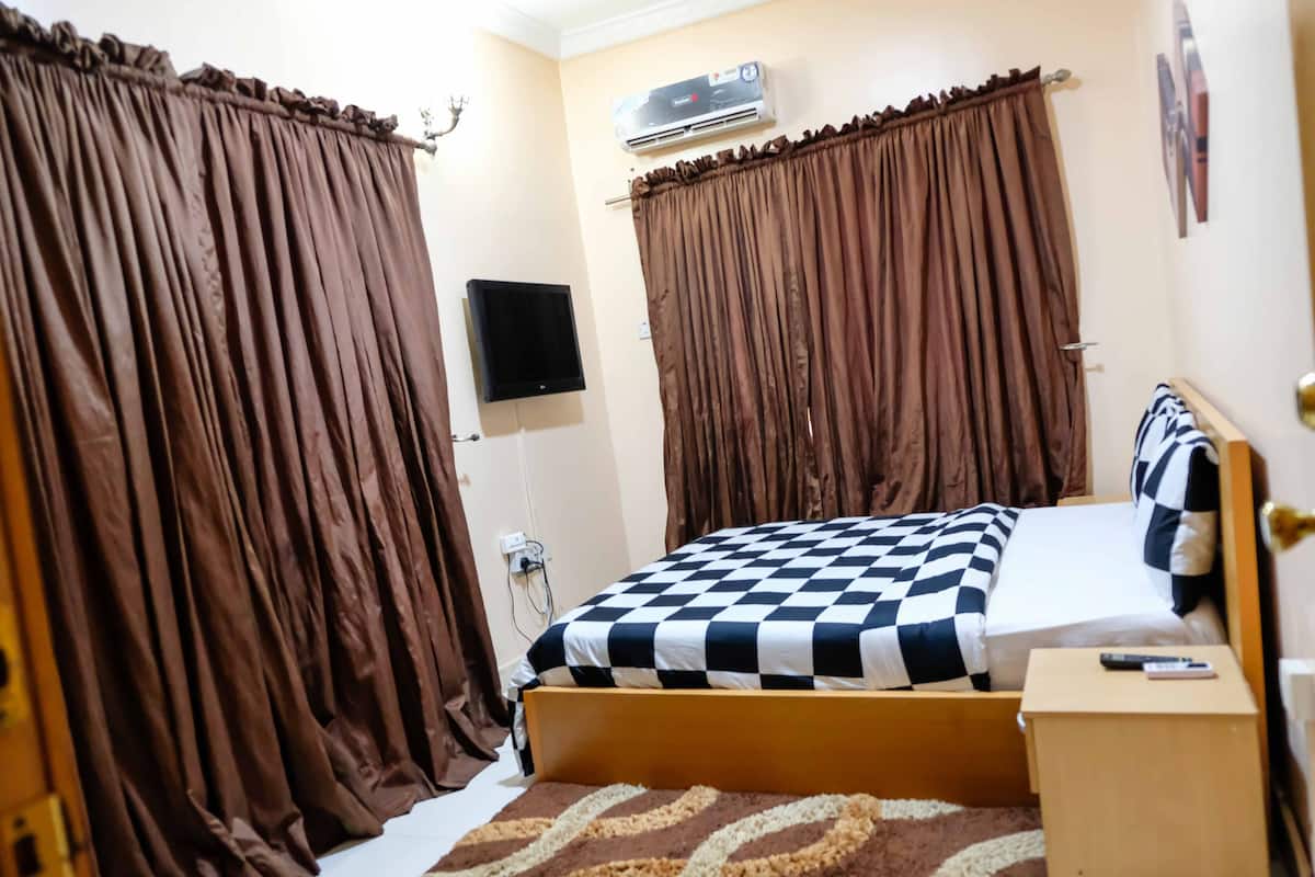 A bedroom with a bed, curtains, an air conditioner, a TV, and a bedside table.