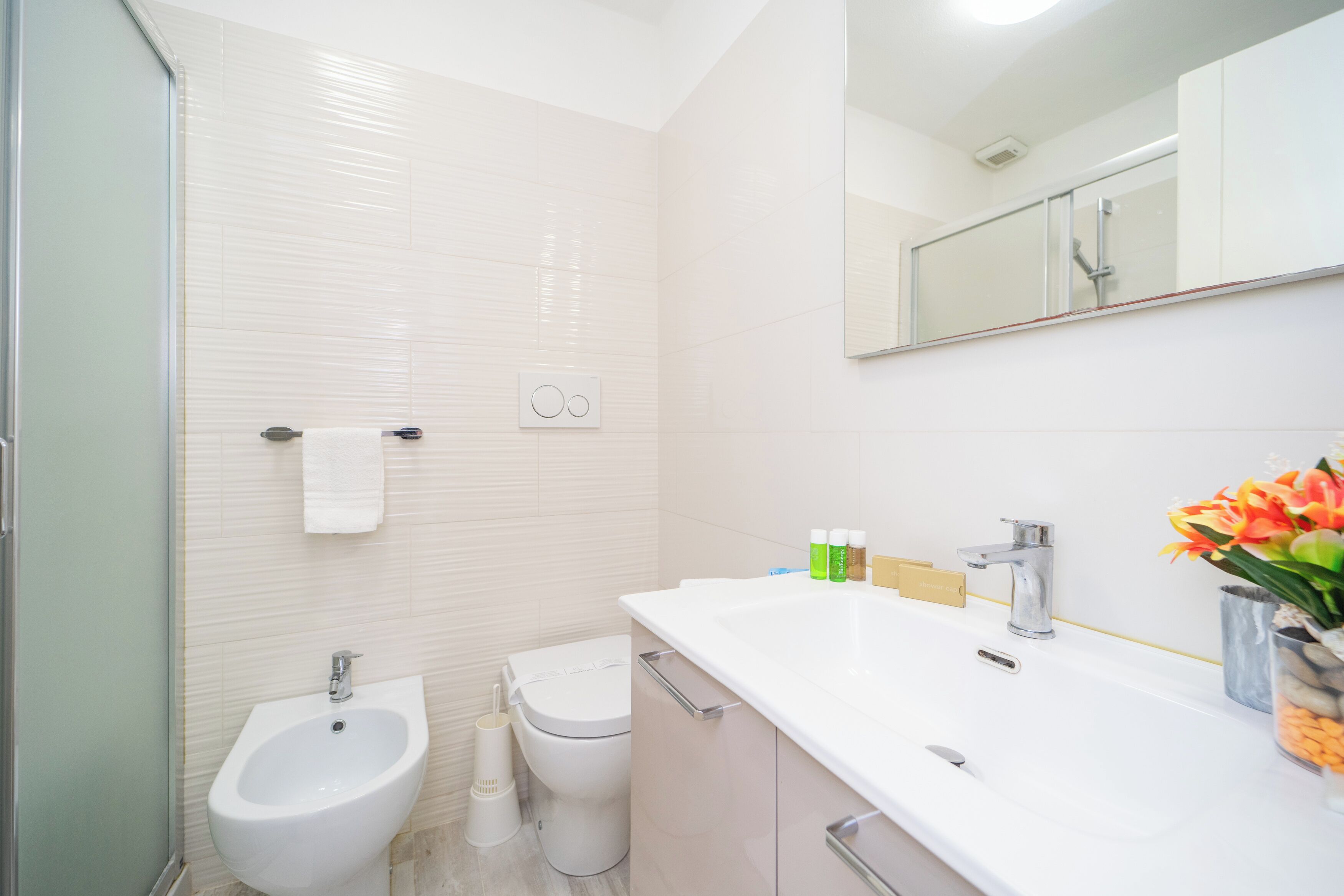 Een moderne badkamer met een bidet, toilet en een grote witte wastafel met spiegel erboven.