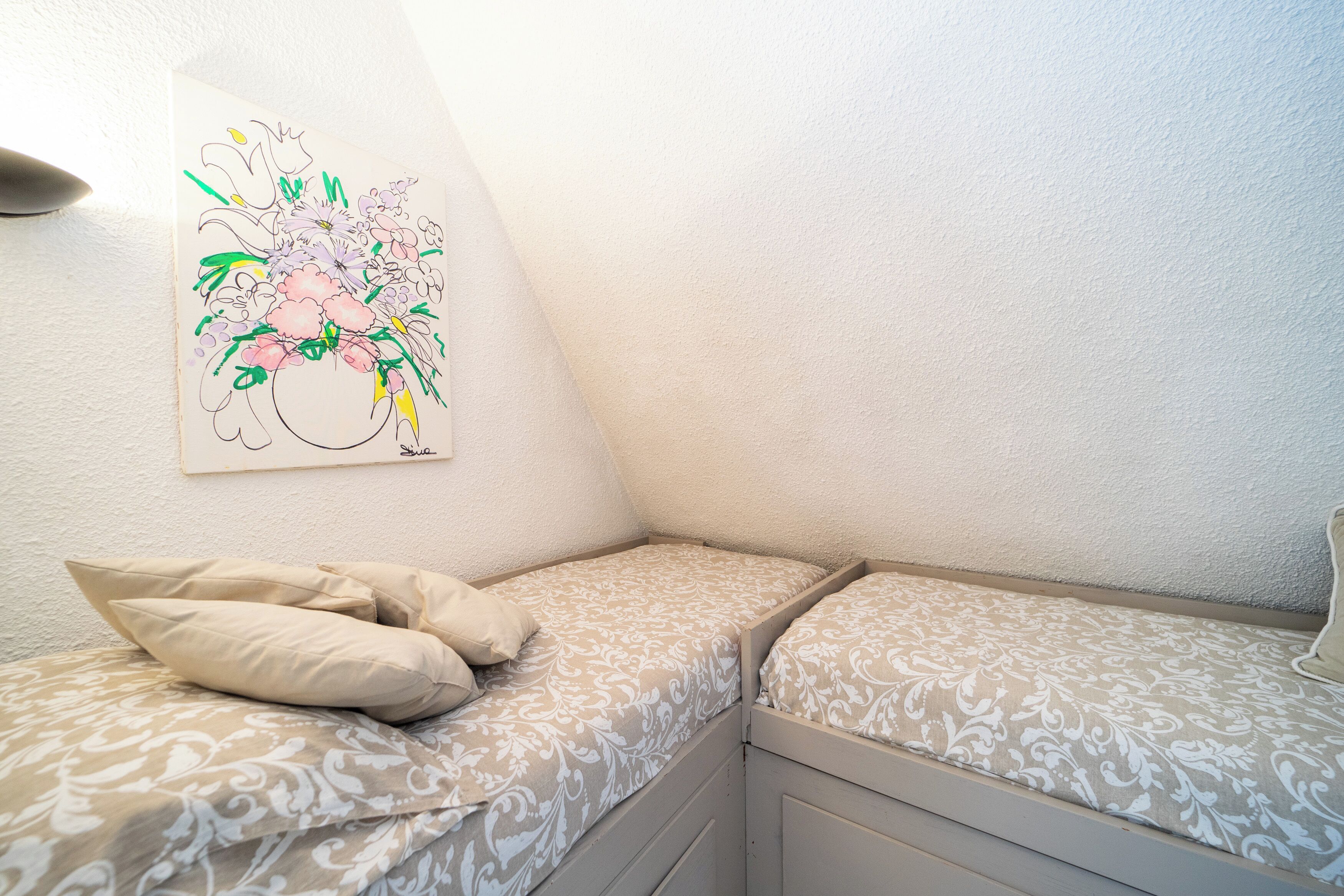 Une chambre d’angle avec deux lits, une œuvre d’art accrochée au mur et un mur blanc à la texture particulière.