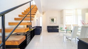 Un espacio habitable moderno con una escalera de madera, una mesa de comedor de vidrio y un sofá de color oscuro.