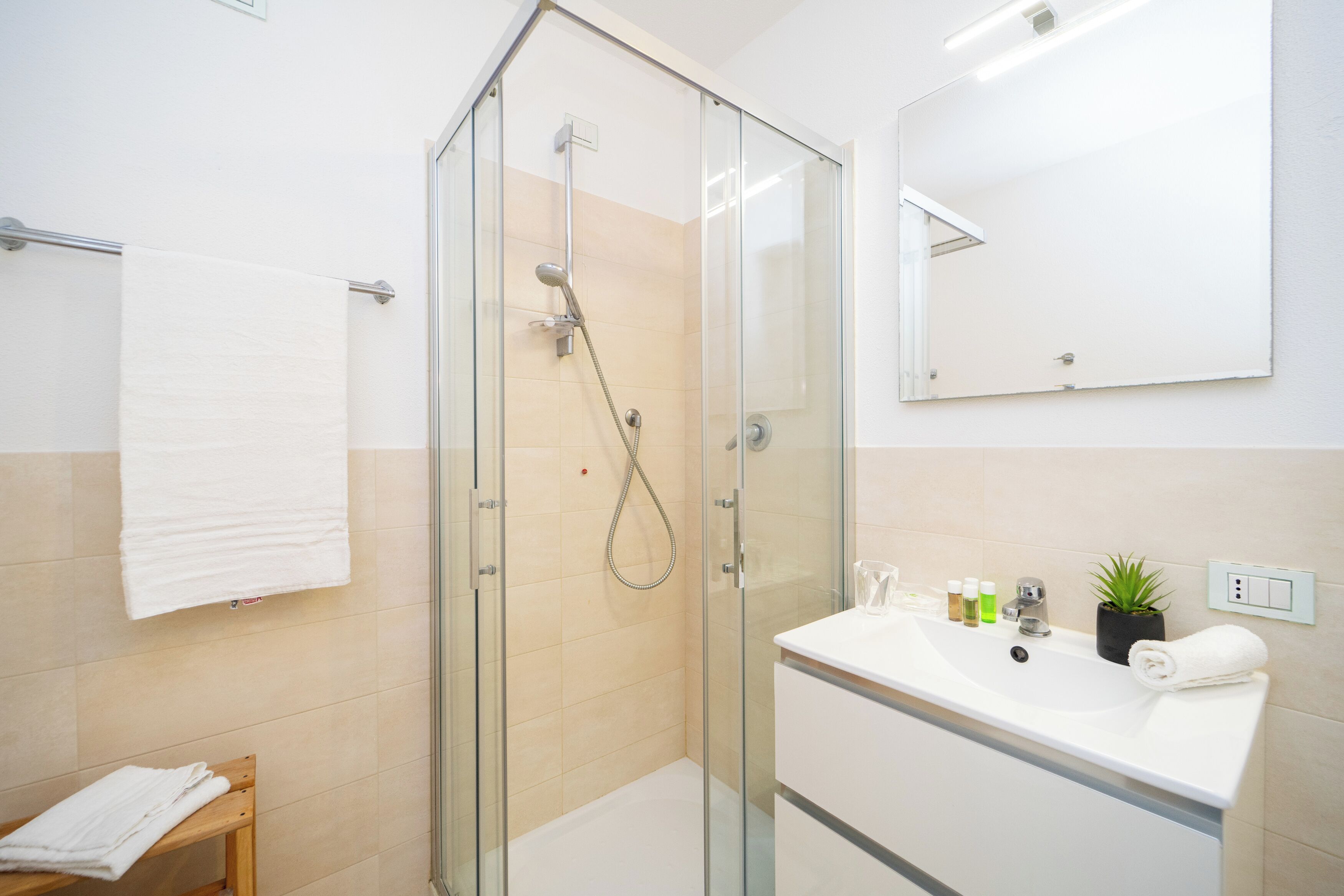 Un baño moderno con ducha de vidrio, lavamanos blanco con artículos de aseo y espejo en la pared.