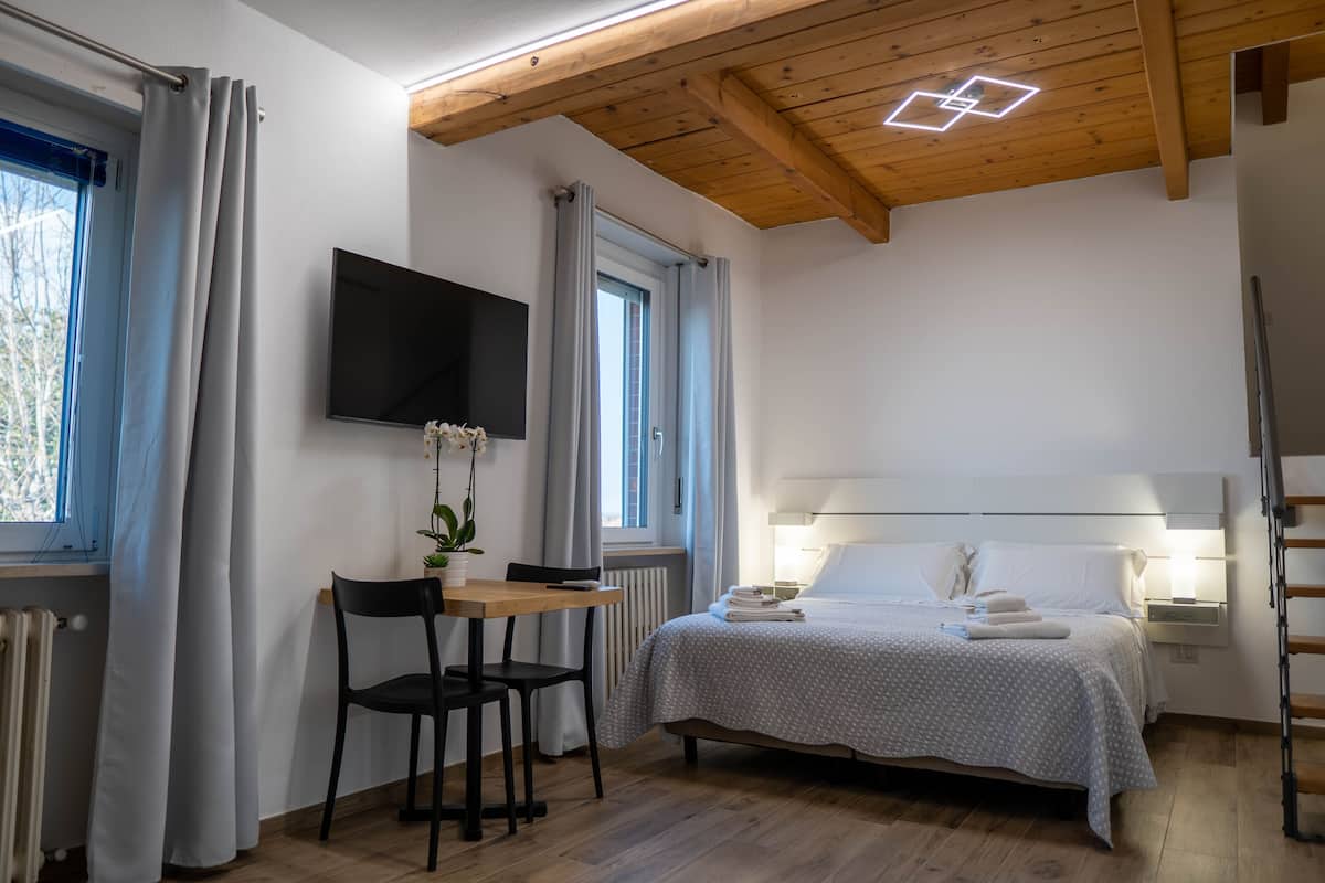 A bedroom with a bed, bedside table, chair, TV, and a window with curtains.