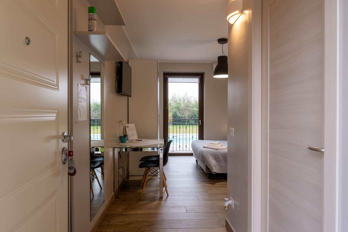 A compact room with a bed, a desk, and a chair. There is a window with a view of greenery outside.