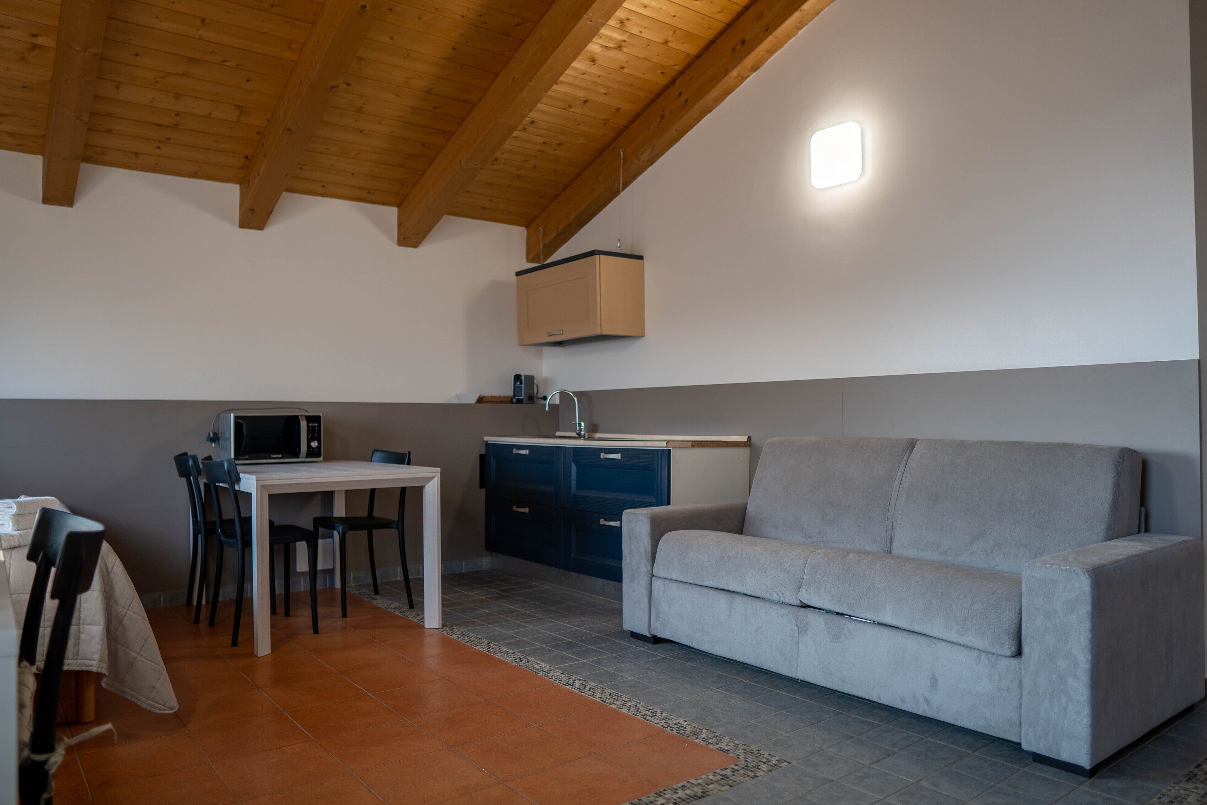 Een ruimtelijke zithoek met een kitchenette, een eettafel met stoelen en een bank.