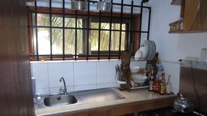 A kitchen with wooden cabinets, a stainless steel sink, a window with a view of palm trees, and a stove. - Kwesi Affum Apartments (Accra)
