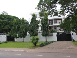 Un bâtiment moderne à deux étages, avec une façade blanche, une entrée sécurisée par un portail et une allée pavée.