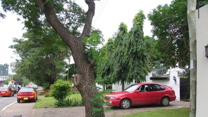 A red car parked on a paved driveway next to a tree. - Kwesi Affum Apartments (Accra)