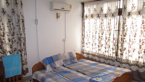 A bedroom with a wooden bed, floral curtains, and an air conditioning unit on the wall. - Kwesi Affum Apartments (Accra)
