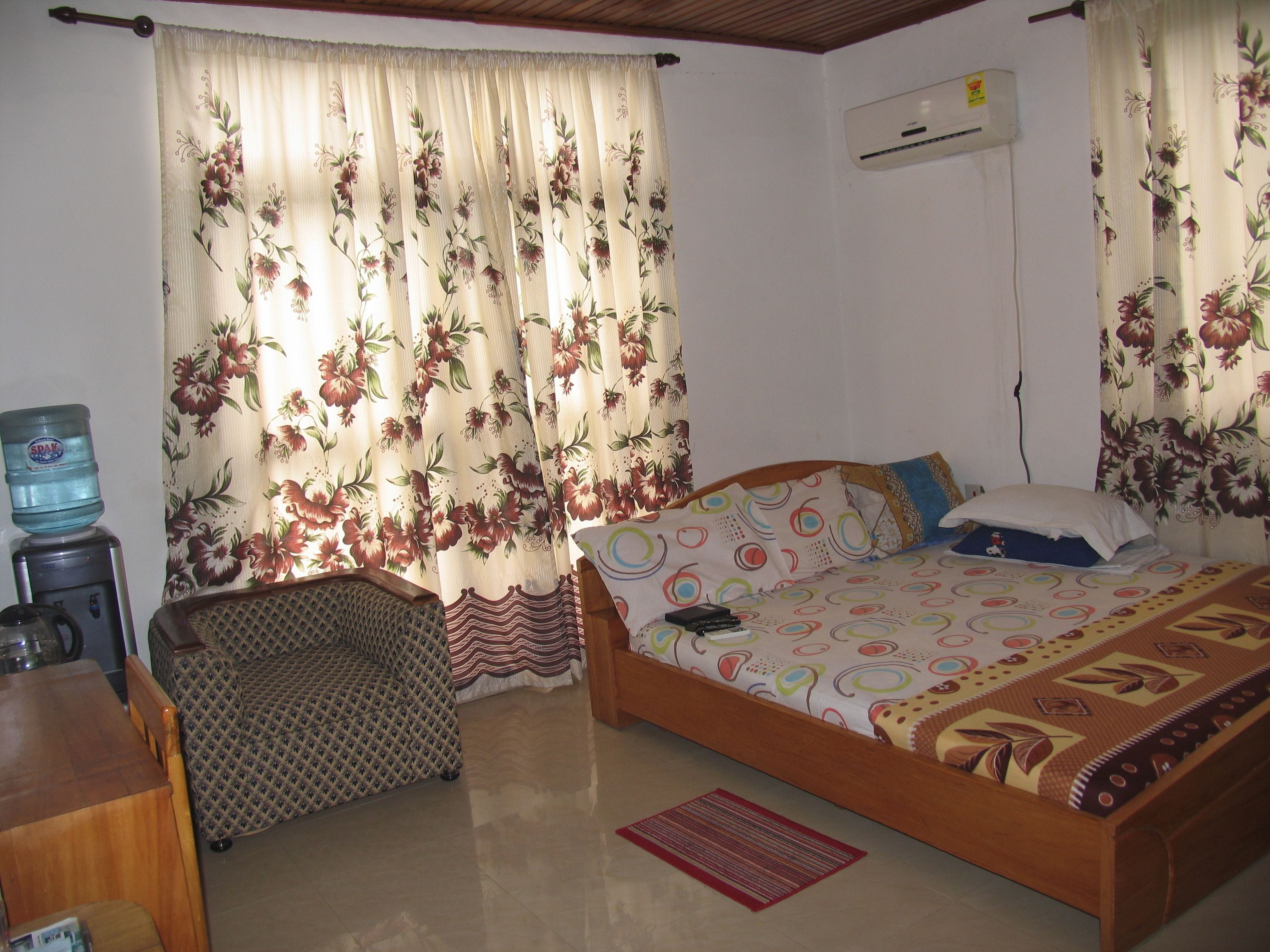 A bedroom with a bed, a chair, a water dispenser, and an air conditioning unit.