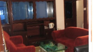 A living room with two red sofas, a glass coffee table, and a wooden cabinet with a kettle on top. - Kwesi Affum Apartments (Accra)