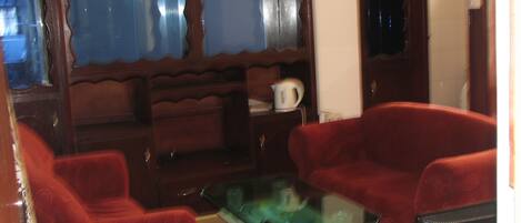 A living room with two red sofas, a glass coffee table, and a wooden cabinet with a kettle on top.