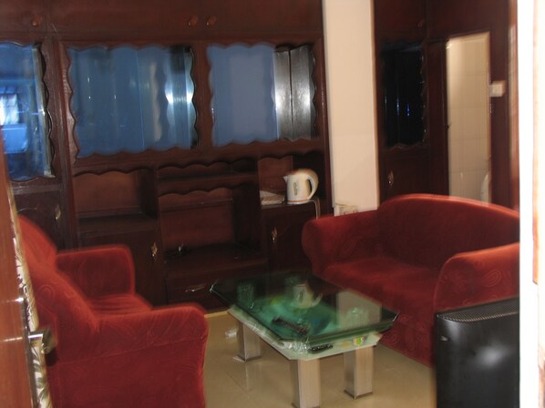 A living room with two red sofas, a glass coffee table, and a wooden cabinet with a kettle on top.