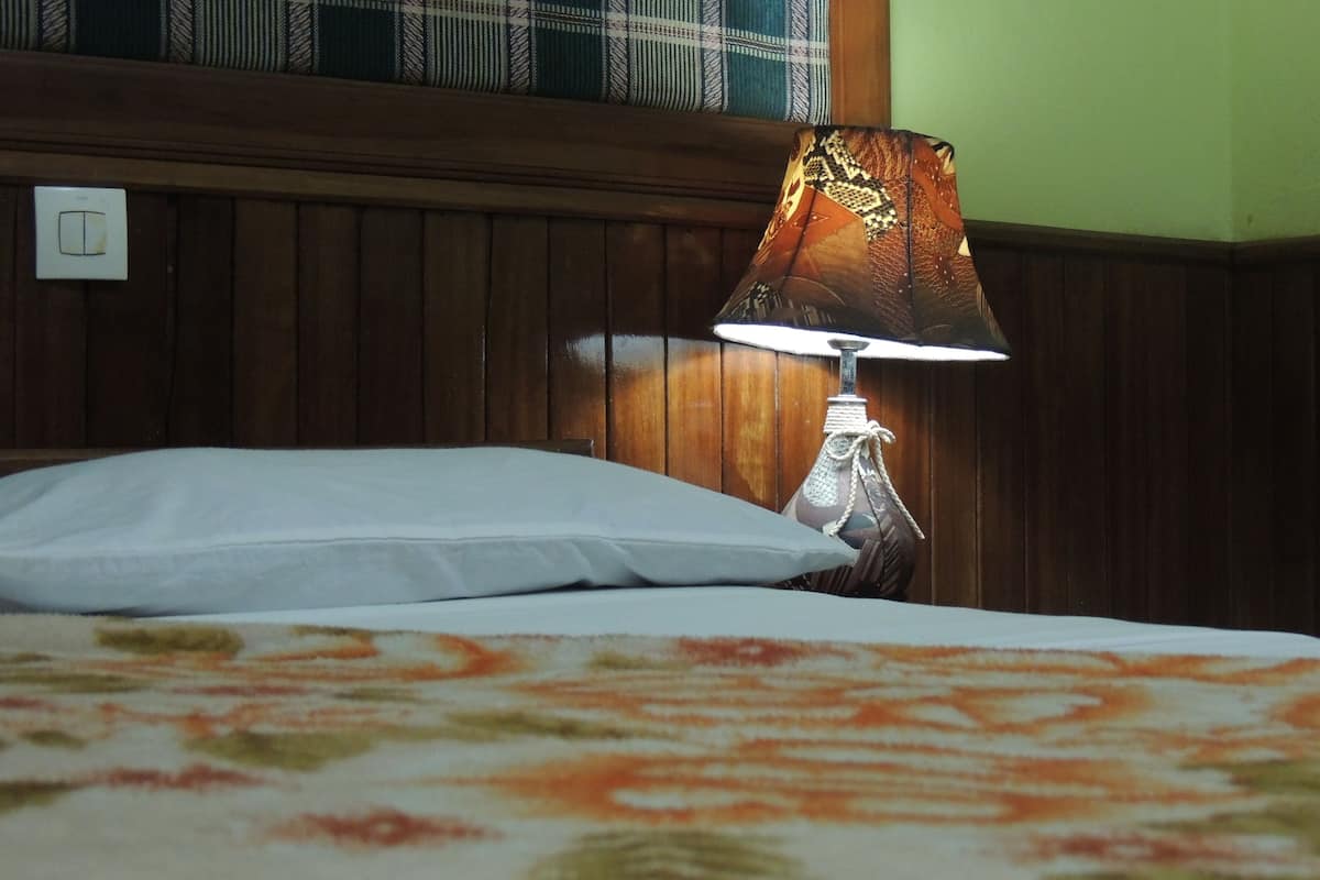 A bed with a floral-patterned bedspread, a white pillow, and a table lamp with a patterned lampshade.