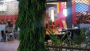 An outdoor seating area with metal chairs and tables, surrounded by a decorative fence and greenery. - Saffana Hôtel (Douala)