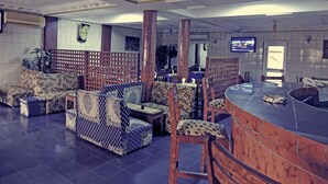 A spacious lobby with patterned sofas, a reception area with a counter, and a television mounted on the wall. - Saffana Hôtel (Douala)