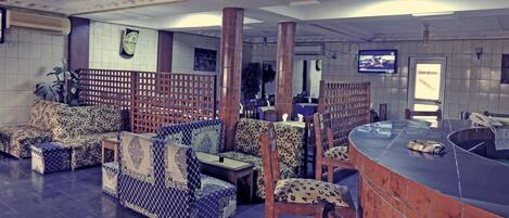 A spacious lobby with patterned sofas, a reception area with a counter, and a television mounted on the wall.