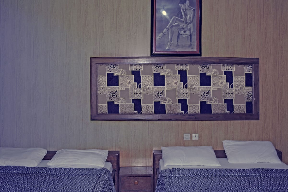 A hotel room with two beds, a framed artwork above the beds, and a decorative panel on the wall.