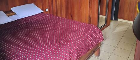 A room with a wooden headboard, a bed with a red patterned bedspread, a mirror, and a chair.