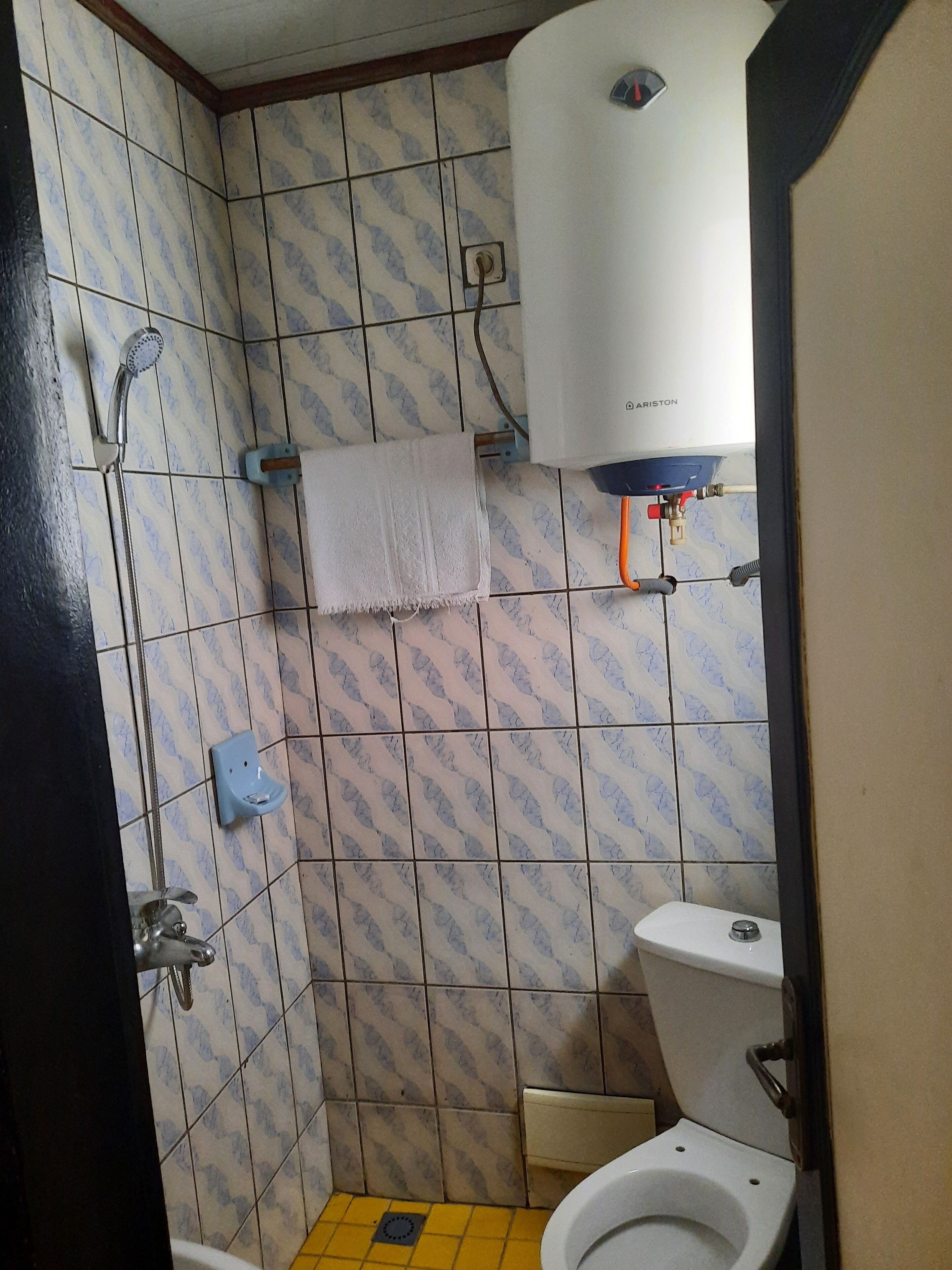 A small bathroom with a toilet, a shower, and a towel hanging on the wall.