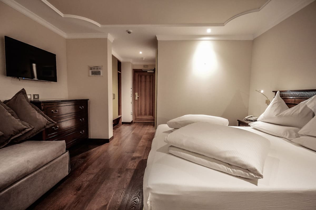 Una habitación de hotel con una cama, un sofá, un aparador y un televisor montado en la pared.