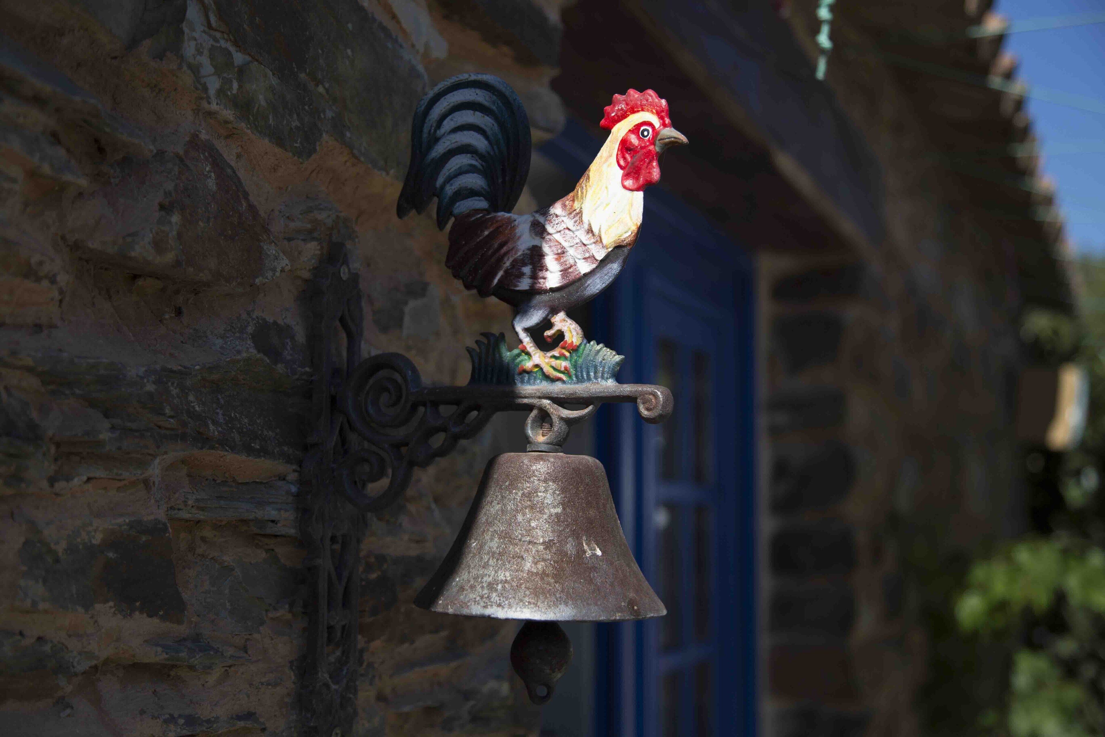 Una figurina de gallo montada en una pared con una campana colgando debajo.