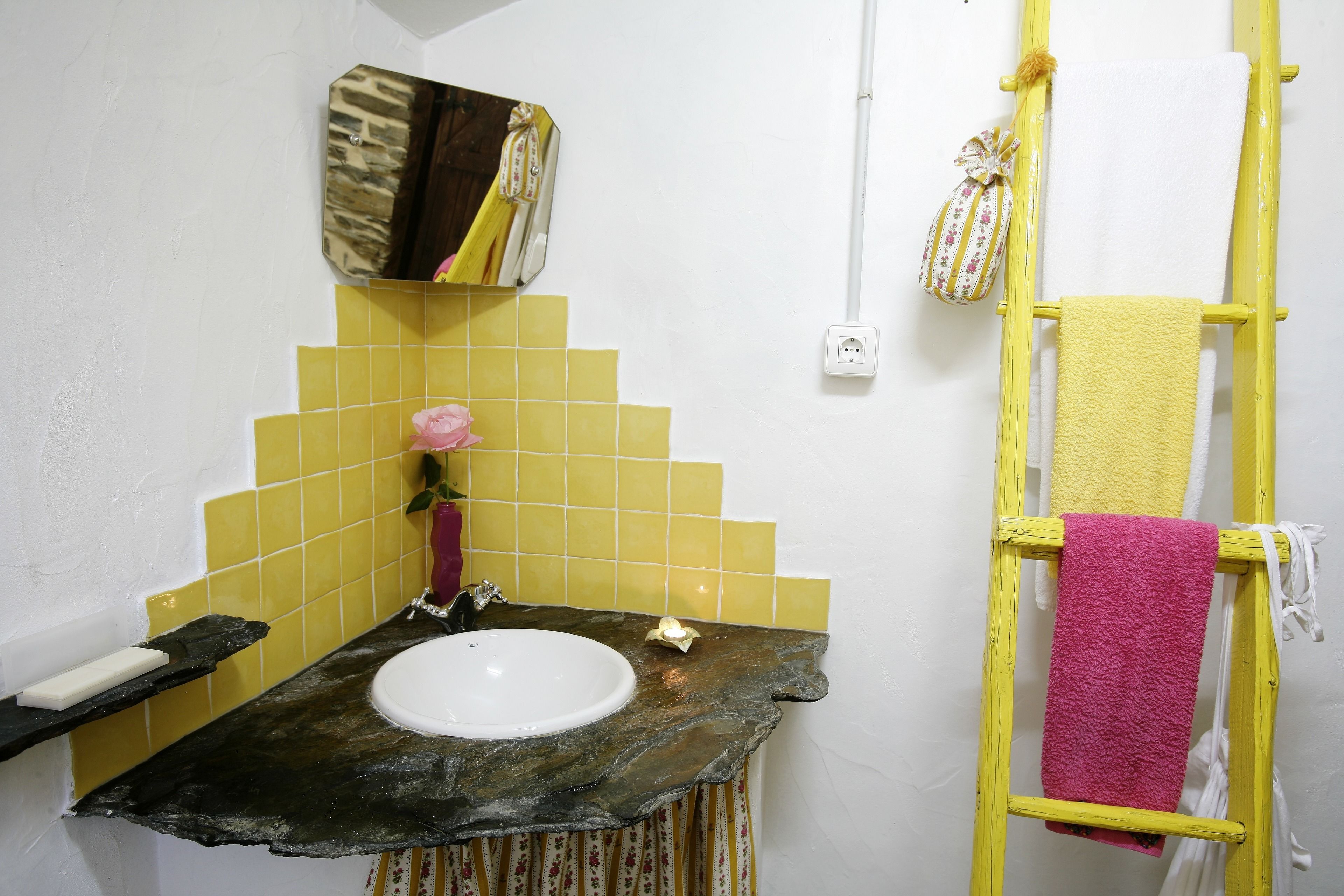 Un baño con lavamanos, azulejos amarillos, un espejo y un perchero amarillo.