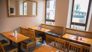 Un restaurant avec des tables et des chaises en bois, un grand miroir au mur et de grandes fenêtres donnant sur la rue.