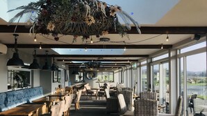 A restaurant with a long counter, wicker chairs, and hanging plants.