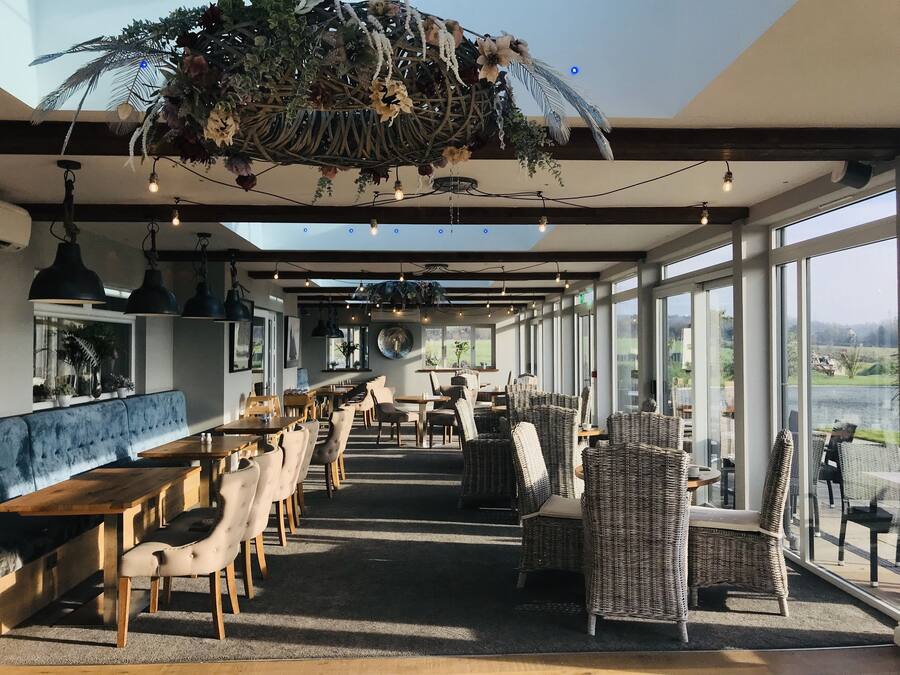 Un restaurant avec un long comptoir, des chaises en osier et des plantes suspendues.