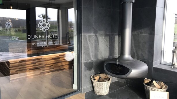 A modern hotel lobby with a reception desk, a large fireplace, and a view of the outdoors.