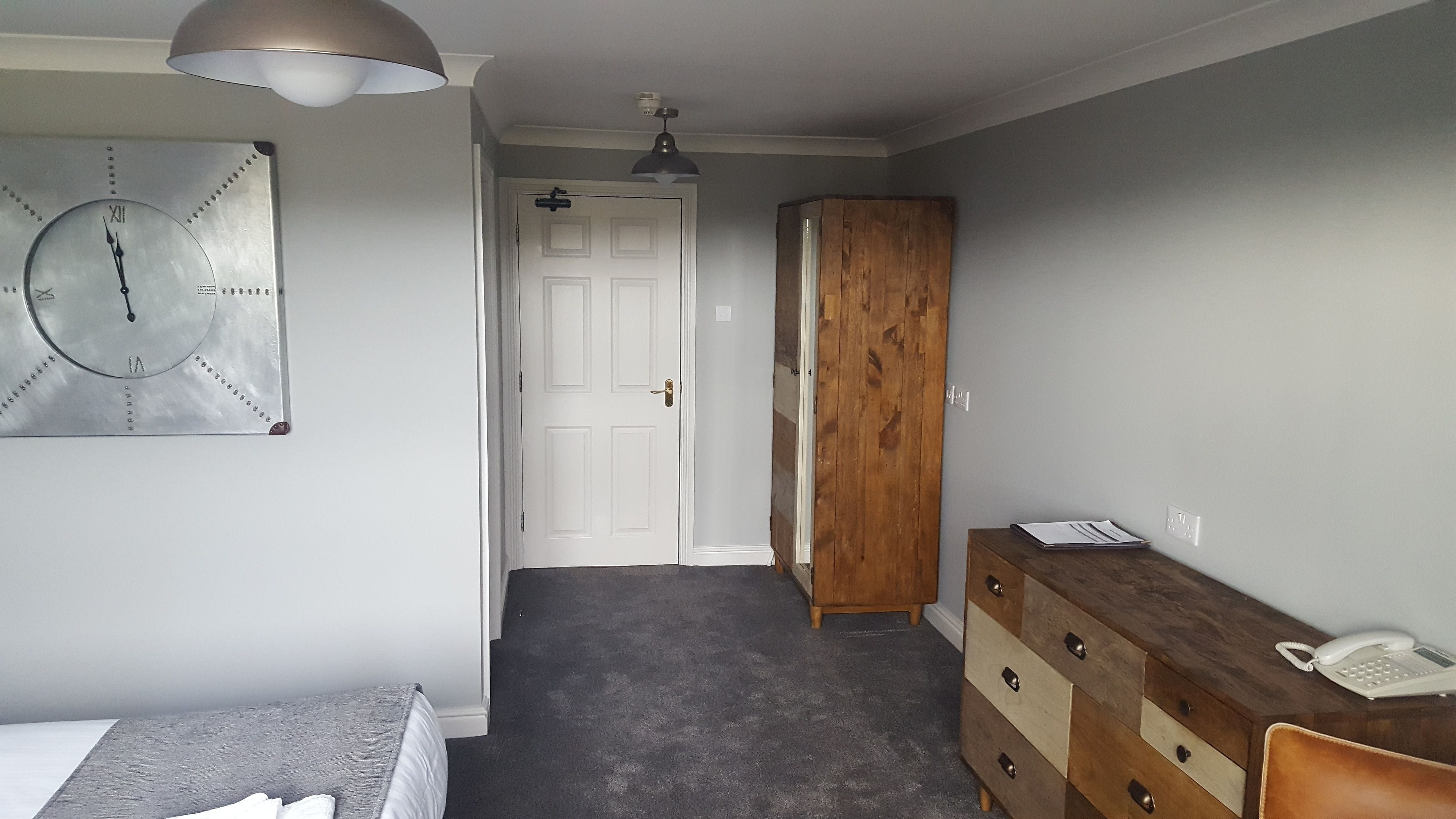 A bedroom with a bed, a dresser, a wooden wardrobe, a clock, and a ceiling fan.