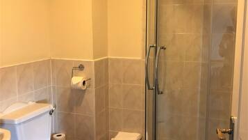 Un baño con inodoro, cabina de ducha de vidrio y lavamanos blanco.