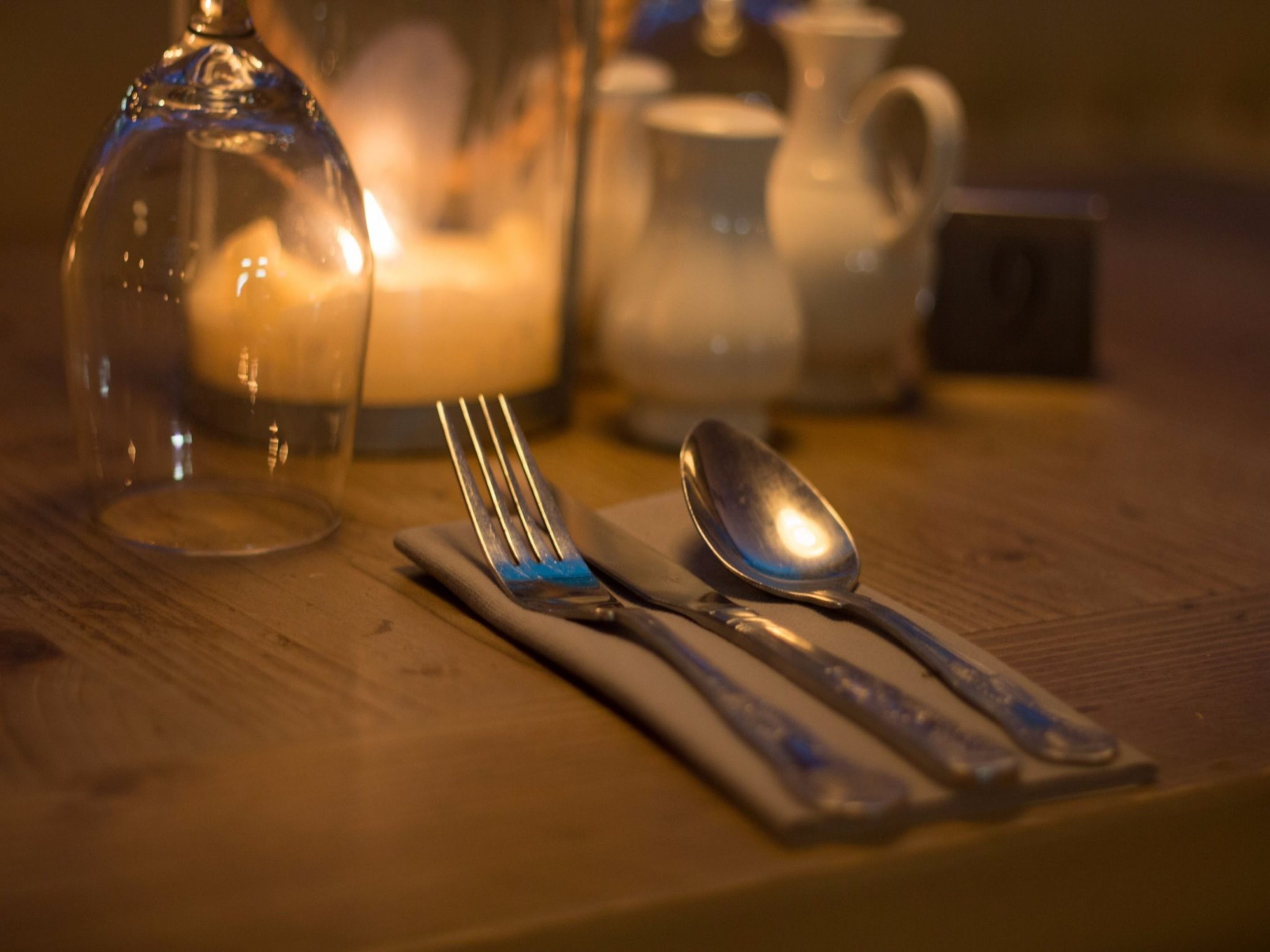 A table set with a fork, spoon, and knife, a glass pitcher, and a candle.