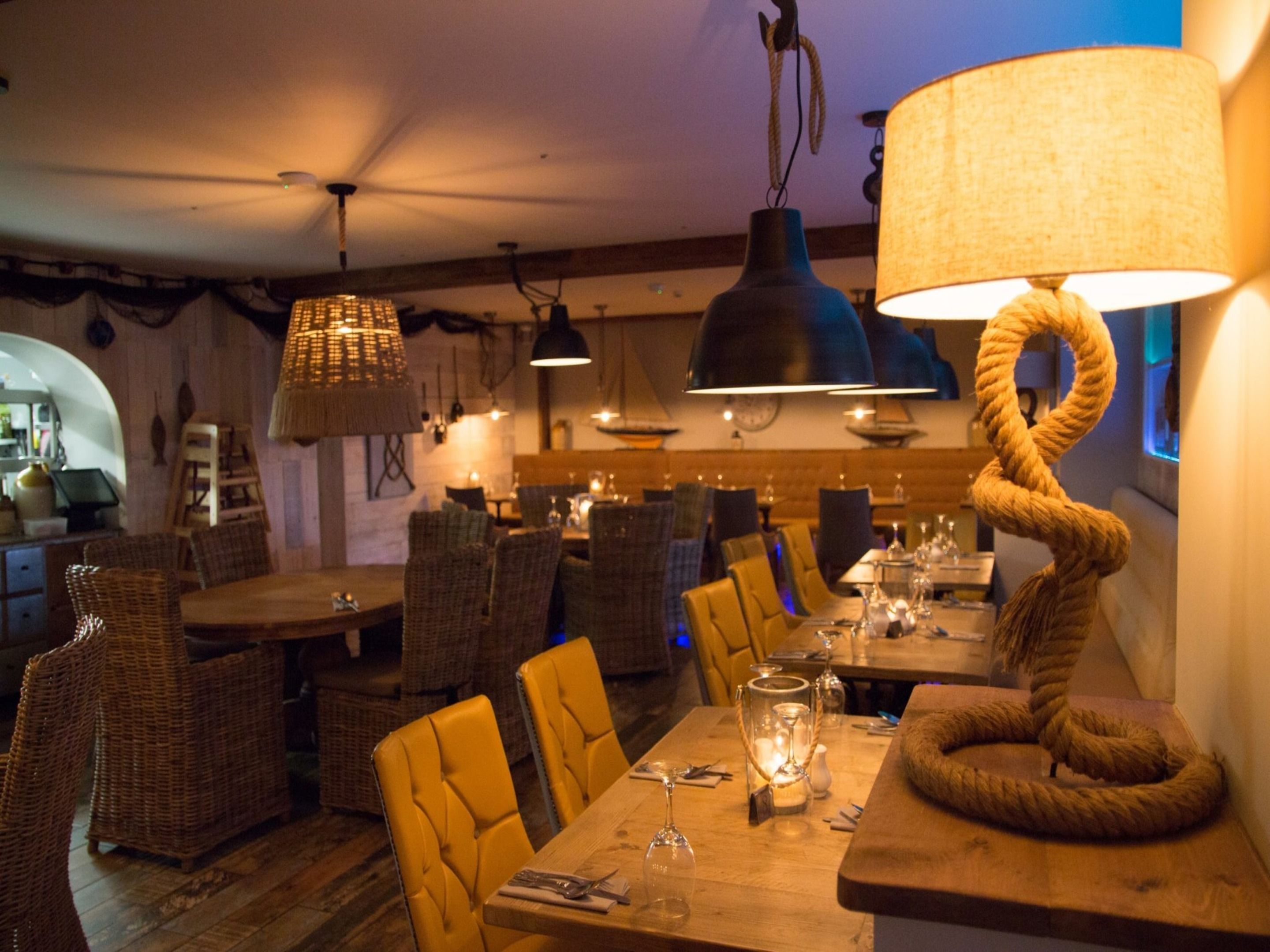 A restaurant interior with wicker chairs, wooden tables, and hanging pendant lights.