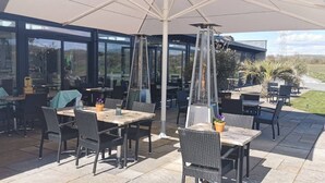 An outdoor patio with tables and chairs, a large umbrella, and a view of the surrounding landscape.