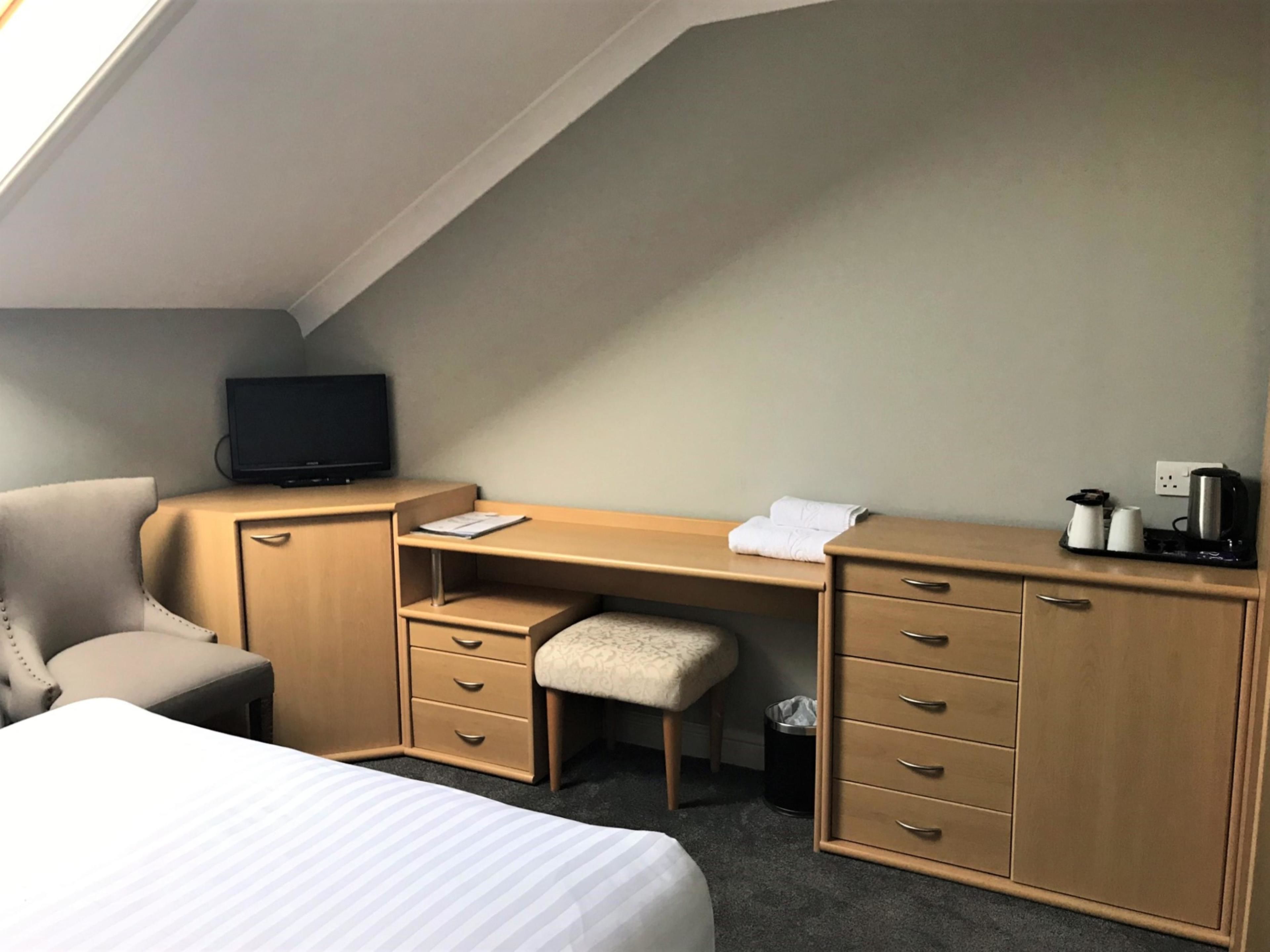 Una habitación de hotel con cama, escritorio, silla, televisor y cubo de basura.