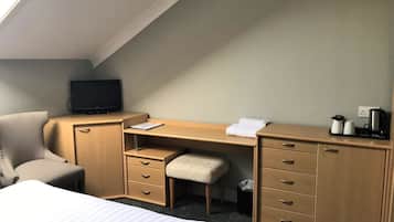 Una habitación de hotel con cama, escritorio, silla, televisor y cubo de basura.