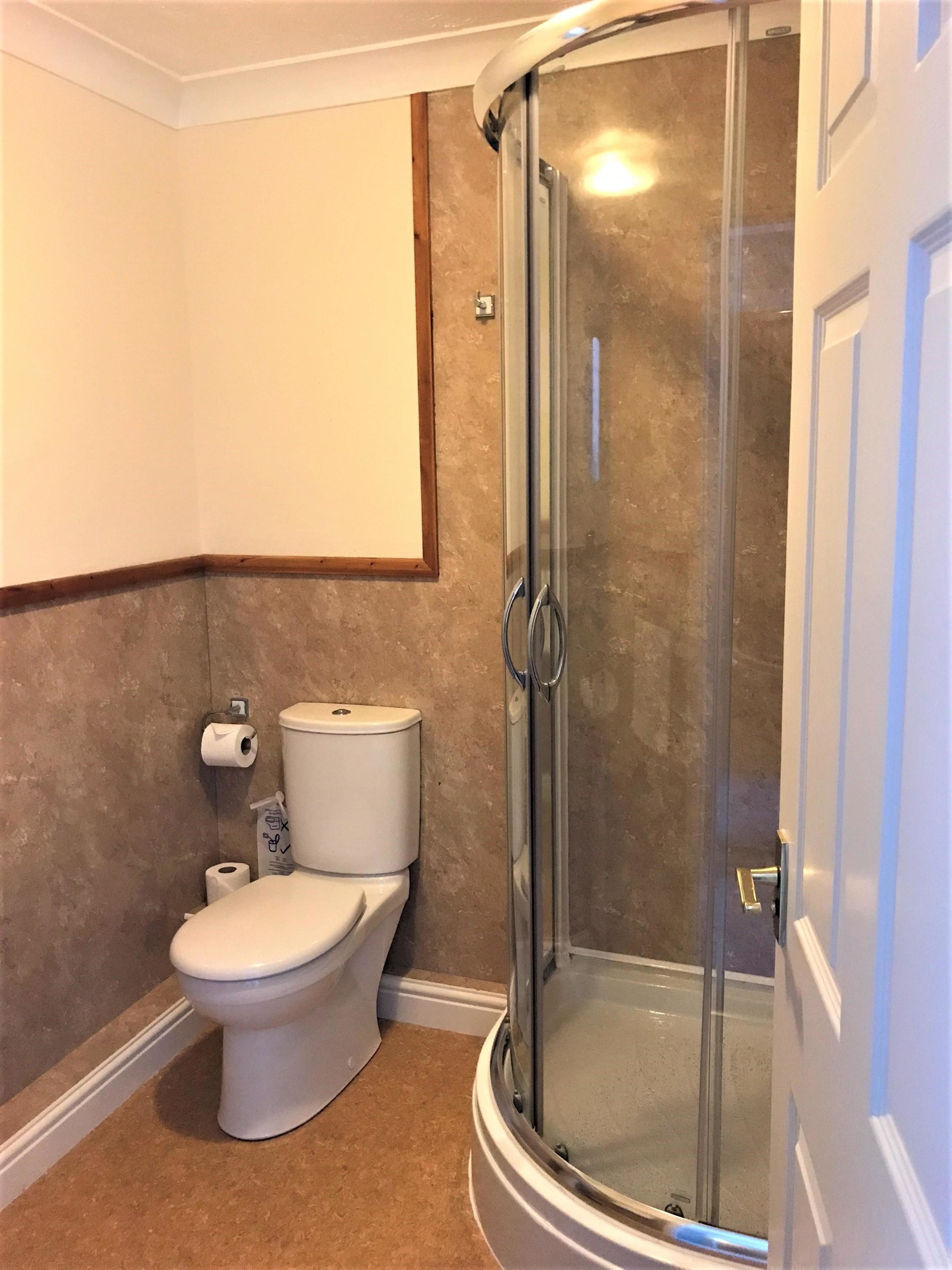 Un baño con inodoro, cabina de ducha de cristal y toallero.