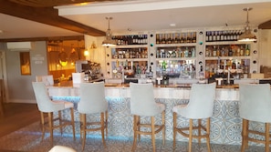 A bar area with multiple stools and a variety of liquor bottles. - The Dunes Hotel (Barrow-in-Furness)