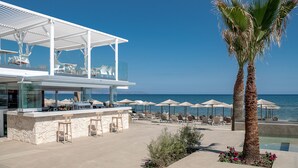 A beachfront bar with outdoor seating, palm trees, and a view of the sea. - Sea Front Villas (Chania)
