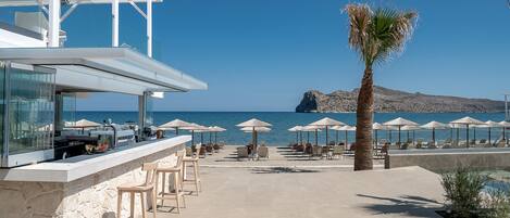 A seaside bar area with outdoor seating, a pool, and a view of the sea.