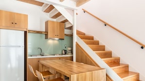 A modern kitchen with wooden cabinets, a built-in stove, and a wooden dining table with bar stools. - Sea Front Villas (Chania)