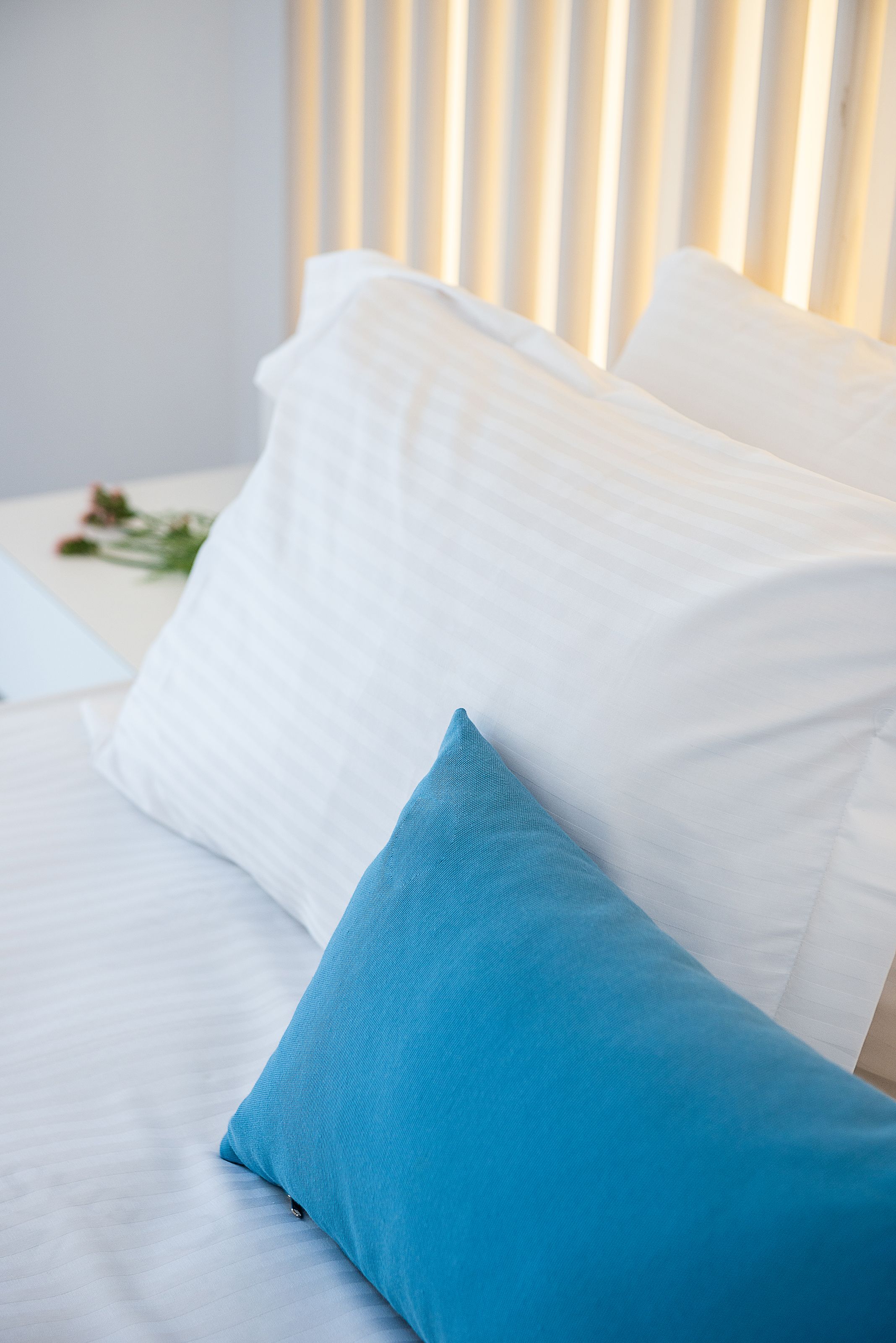 A bed with white bedding and a single blue pillow.