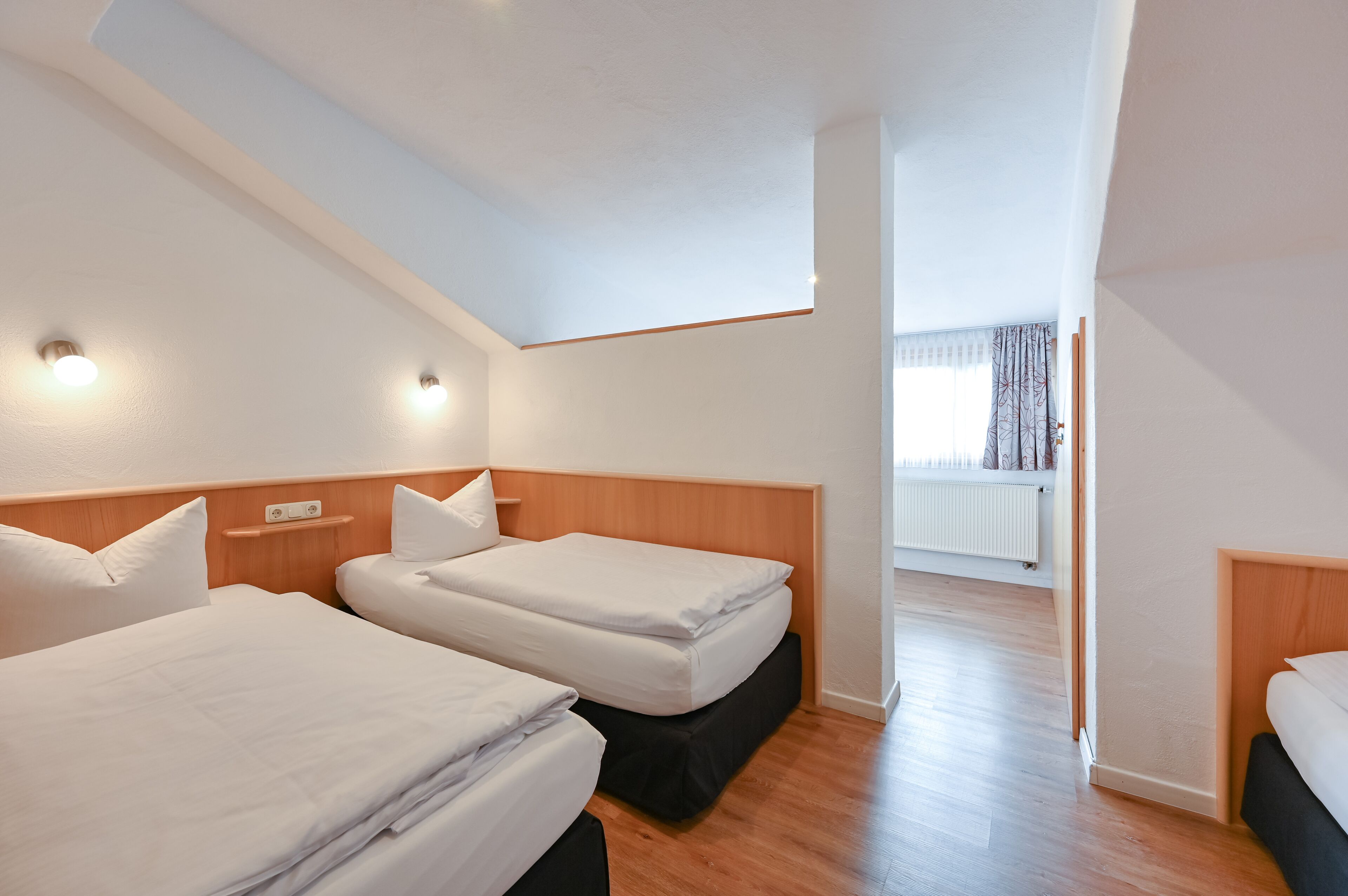 A hotel room with two single beds, a wooden headboard, a small shelf, and a view of a balcony.