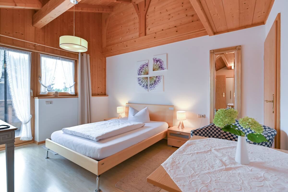 A bedroom with a wooden ceiling, a bed with white bedding, two bedside tables with lamps, a mirror, and artwork on the wall.