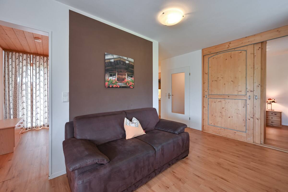 A living room with a brown leather sofa, a wooden wardrobe, and a framed picture on the wall.