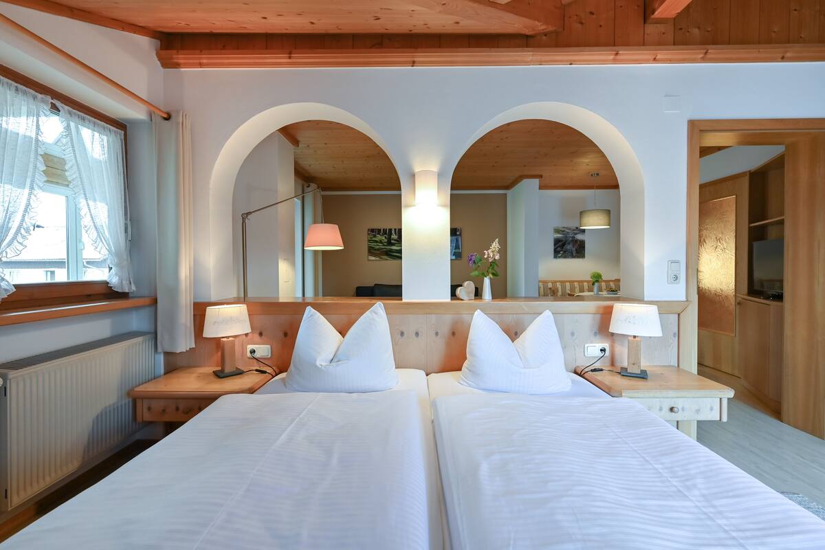 A hotel room with two beds, a wooden headboard, a large mirror, and a window with curtains.