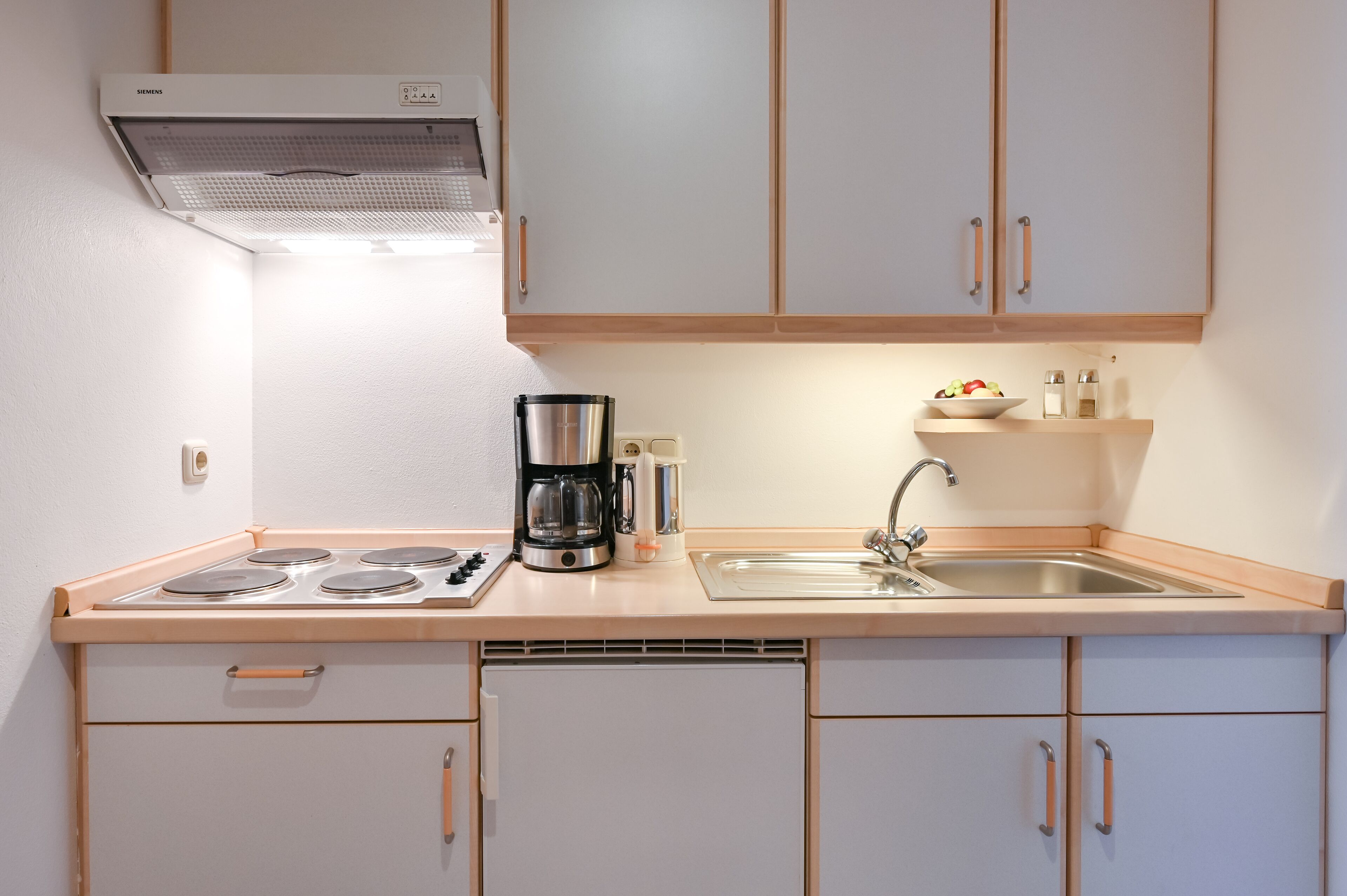 A compact kitchen with a gas stove, coffee maker, and a sink.