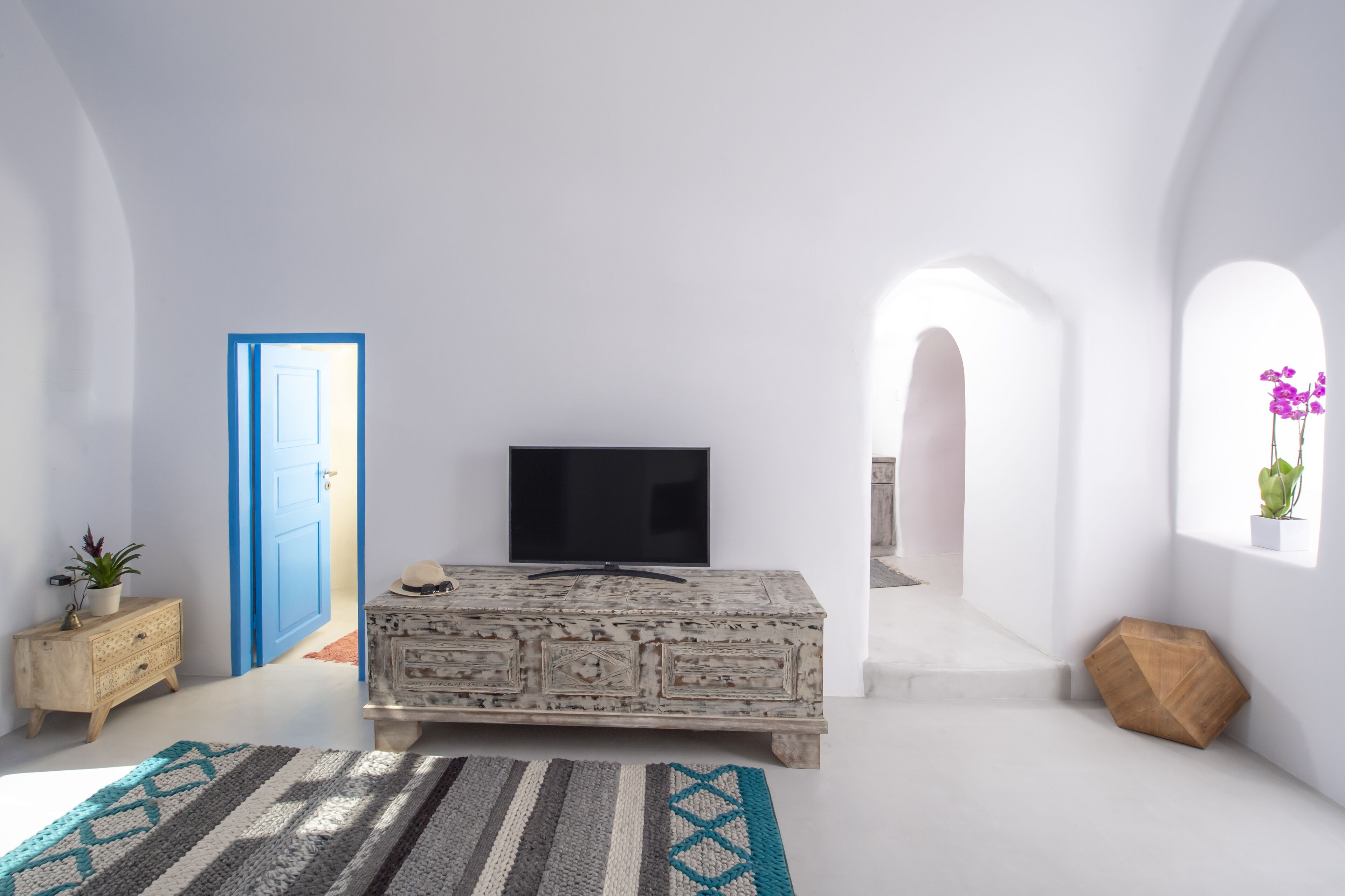 Ein Zimmer mit einem großen Flachbildfernseher auf einem weißen Schrank, einer blauen Tür und einem Fenster mit einer Pflanze.