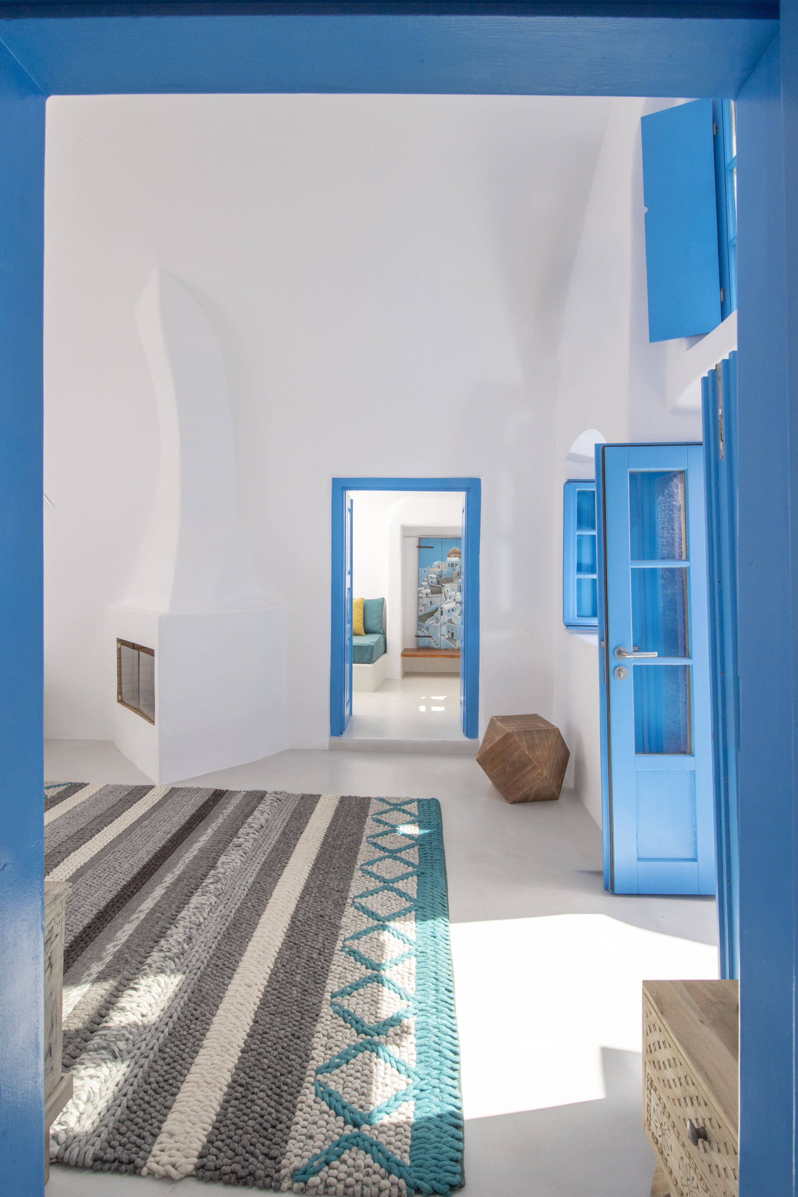 A modern interior with a geometric rug, a wooden bench, and a blue door.